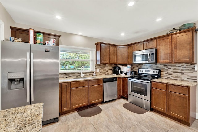 kitchen with sink, backsplash, light stone counters, light tile patterned floors, and appliances with stainless steel finishes