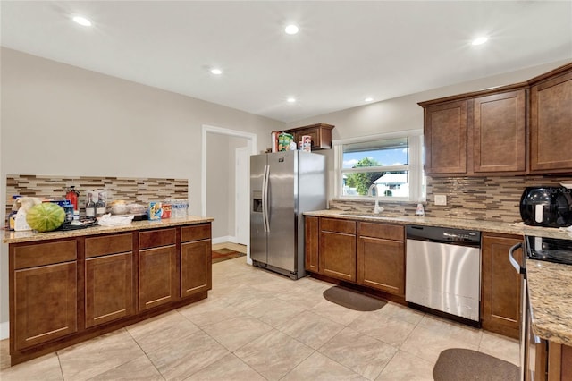 kitchen featuring appliances with stainless steel finishes, light stone countertops, backsplash, and sink