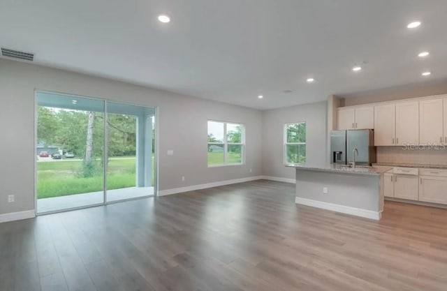 kitchen featuring light hardwood / wood-style flooring, white cabinetry, stainless steel fridge with ice dispenser, a kitchen island with sink, and tasteful backsplash