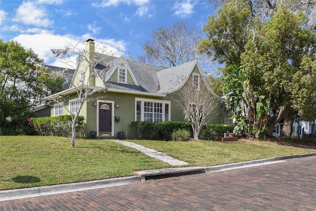 view of front of property featuring a front yard, a chimney, and stucco siding