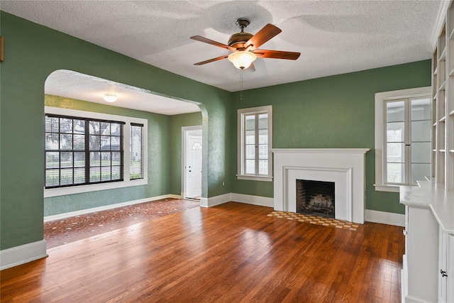 unfurnished living room featuring dark wood-style floors, a textured ceiling, arched walkways, and a fireplace with flush hearth