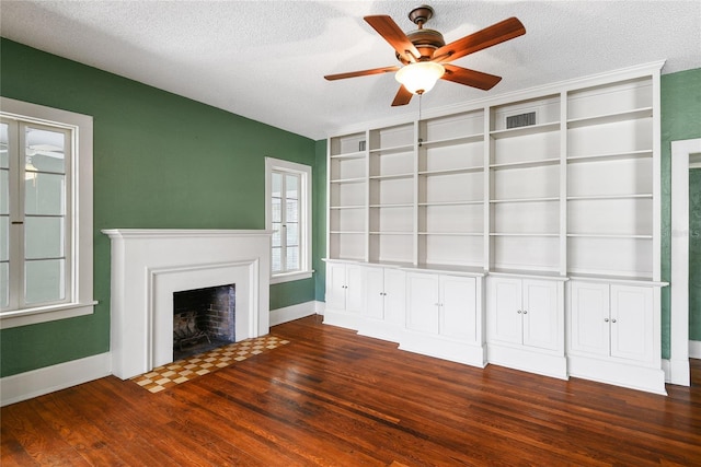 unfurnished living room with a fireplace with flush hearth, dark wood-type flooring, a textured ceiling, and baseboards