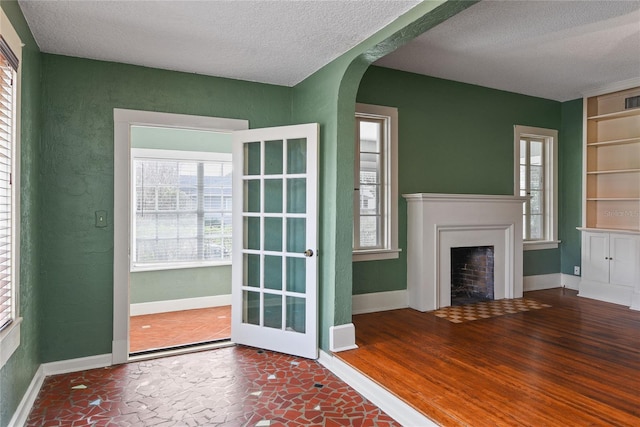 unfurnished living room with a fireplace with flush hearth, arched walkways, plenty of natural light, and wood finished floors