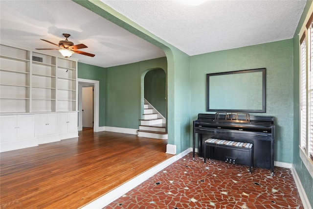 unfurnished living room with baseboards, visible vents, arched walkways, wood finished floors, and a textured ceiling