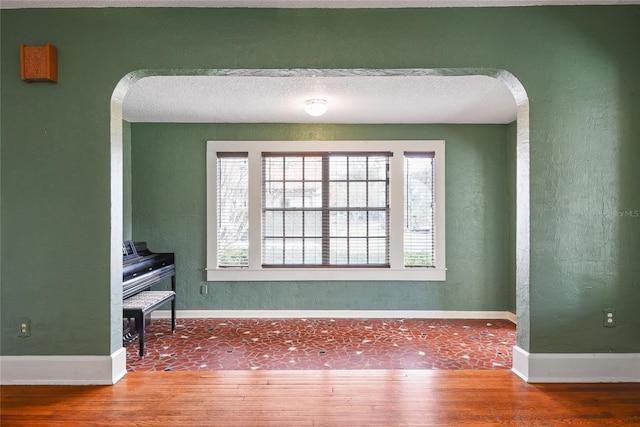 unfurnished room with arched walkways, wood finished floors, and baseboards