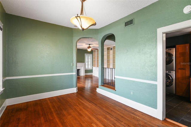 spare room with visible vents, arched walkways, stacked washer / dryer, dark wood-style flooring, and a fireplace