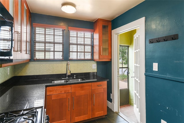 kitchen featuring glass insert cabinets, a sink, backsplash, dark countertops, and stainless steel range with gas stovetop