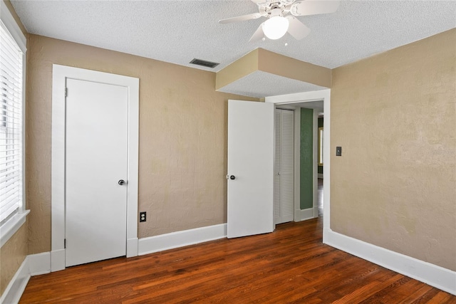 unfurnished bedroom featuring baseboards, dark wood finished floors, a textured ceiling, and a textured wall