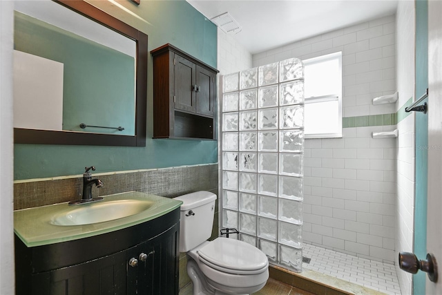 bathroom featuring tile walls, toilet, wainscoting, vanity, and walk in shower