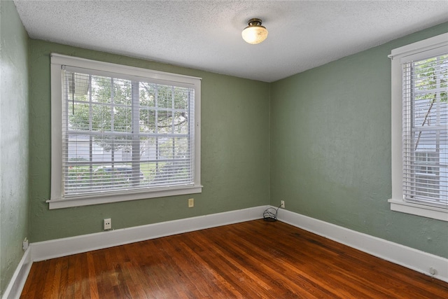 spare room featuring a textured ceiling, wood finished floors, and baseboards