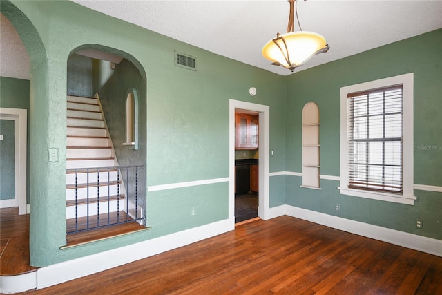 spare room featuring baseboards, visible vents, arched walkways, stairway, and wood finished floors