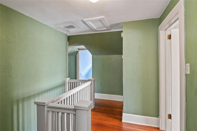 hallway featuring attic access, visible vents, baseboards, wood finished floors, and an upstairs landing