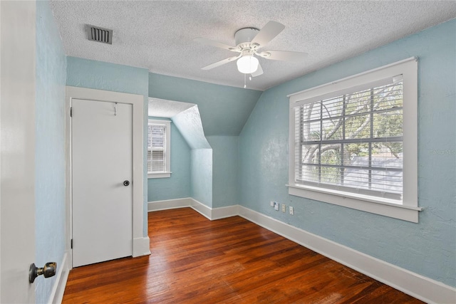 bonus room featuring baseboards, visible vents, dark wood finished floors, vaulted ceiling, and a textured ceiling