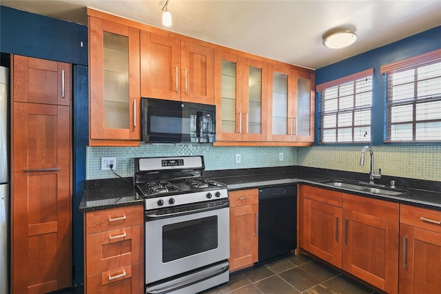 kitchen featuring a sink, dark stone counters, black appliances, tasteful backsplash, and glass insert cabinets