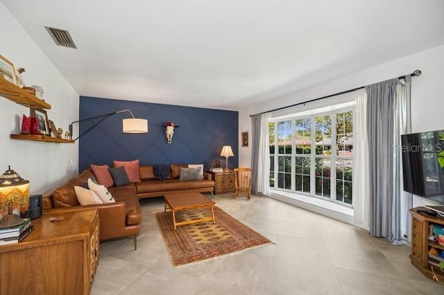 living area with light tile patterned floors, visible vents, and an accent wall