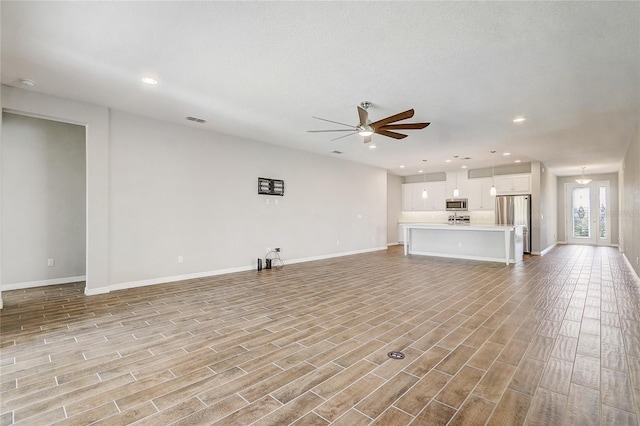 unfurnished living room featuring light wood finished floors, baseboards, visible vents, and a ceiling fan