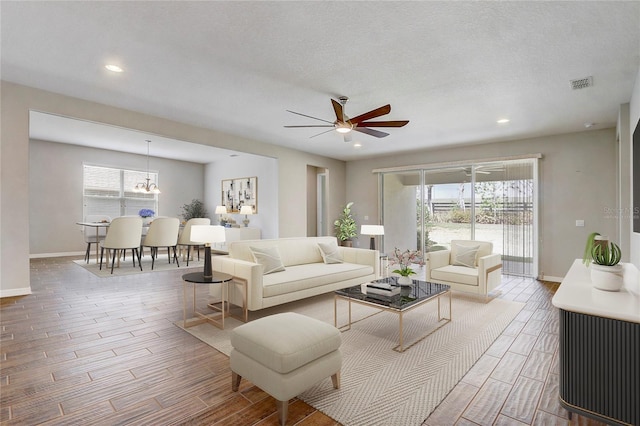 living room featuring visible vents, baseboards, wood tiled floor, ceiling fan with notable chandelier, and recessed lighting