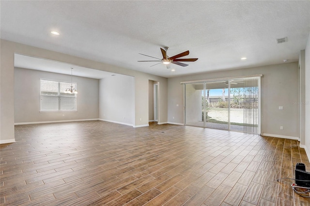 unfurnished room featuring ceiling fan with notable chandelier, wood finished floors, visible vents, and a healthy amount of sunlight