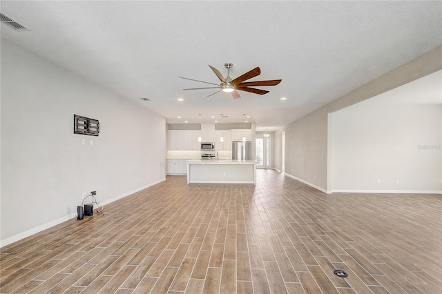 unfurnished living room with a ceiling fan, visible vents, light wood-style flooring, and baseboards