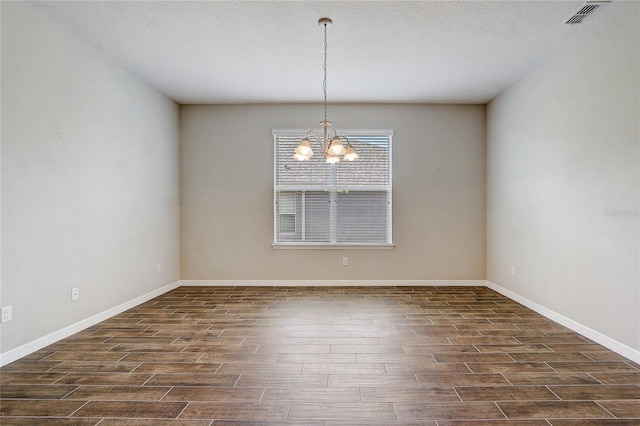 empty room featuring a chandelier, a textured ceiling, dark wood-style flooring, visible vents, and baseboards