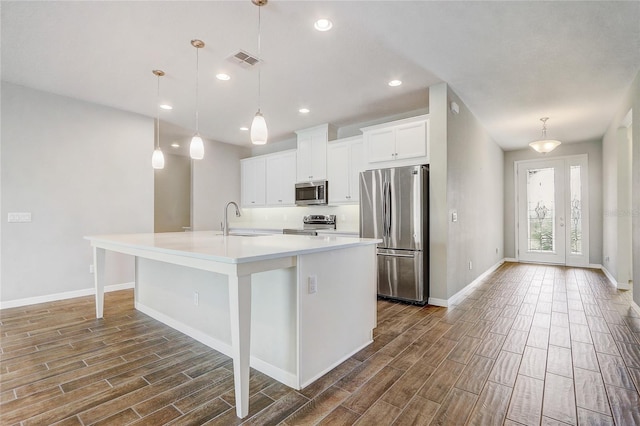 kitchen with a sink, visible vents, hanging light fixtures, appliances with stainless steel finishes, and a center island with sink