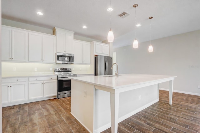 kitchen with a center island with sink, visible vents, hanging light fixtures, stainless steel appliances, and light countertops