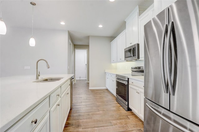 kitchen with pendant lighting, stainless steel appliances, light countertops, white cabinetry, and a sink