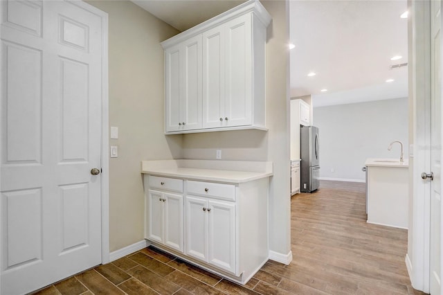 kitchen featuring a sink, white cabinets, light countertops, freestanding refrigerator, and light wood finished floors