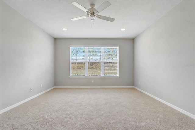 spare room featuring a textured ceiling, light colored carpet, a ceiling fan, and baseboards