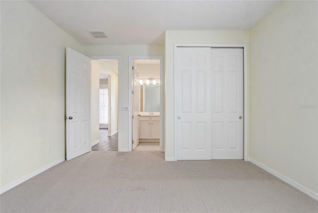 unfurnished bedroom featuring light colored carpet, visible vents, baseboards, a closet, and ensuite bath