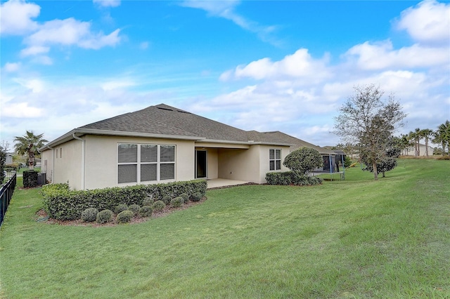 rear view of house with a patio, a shingled roof, fence, a lawn, and stucco siding