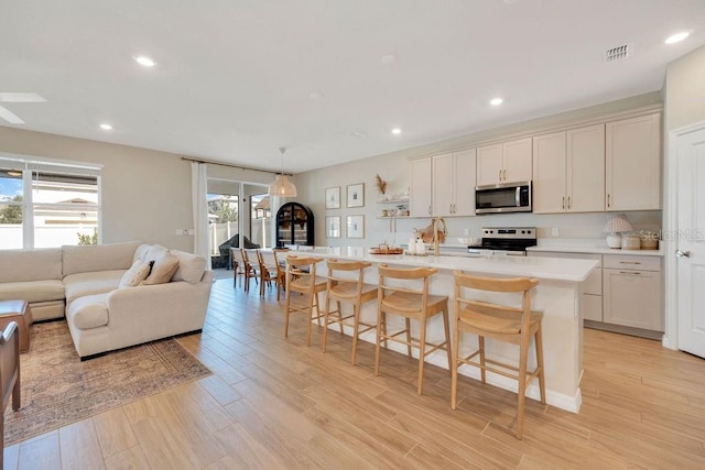 kitchen featuring light countertops, a center island with sink, white cabinets, stainless steel appliances, and a breakfast bar