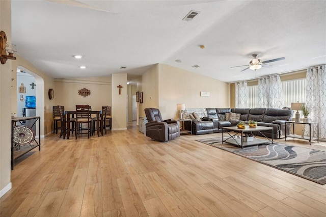 living area featuring arched walkways, light wood finished floors, visible vents, a ceiling fan, and baseboards