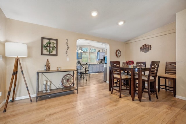 dining area with arched walkways, vaulted ceiling, light wood-style flooring, and baseboards