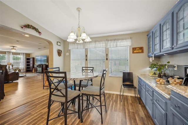 dining area with arched walkways, ceiling fan with notable chandelier, wood finished floors, baseboards, and a glass covered fireplace