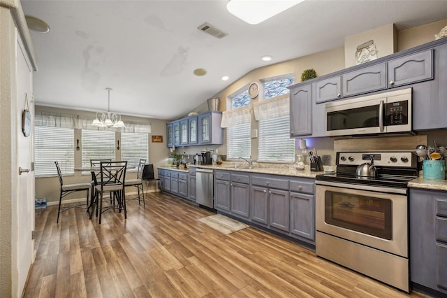 kitchen featuring light wood-style flooring, appliances with stainless steel finishes, decorative light fixtures, gray cabinetry, and a sink