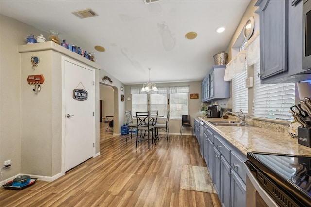 kitchen featuring arched walkways, gray cabinetry, a sink, visible vents, and light wood-type flooring