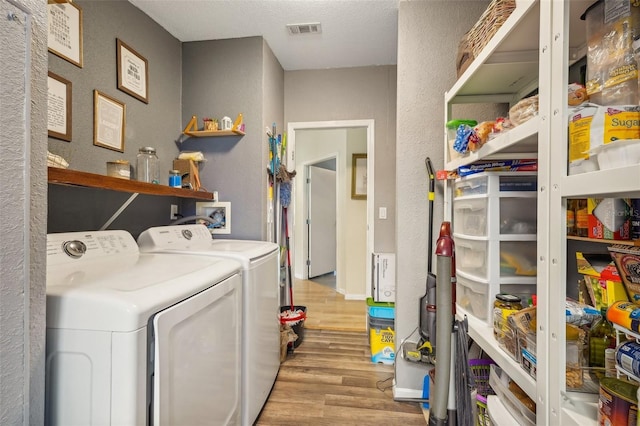 laundry area with laundry area, light wood finished floors, visible vents, a textured wall, and washing machine and clothes dryer