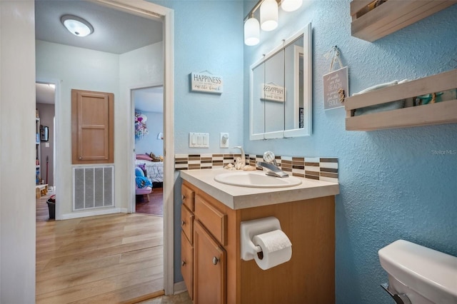 ensuite bathroom featuring visible vents, toilet, vanity, ensuite bath, and wood finished floors