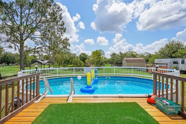 view of swimming pool featuring an outbuilding, a lawn, a wooden deck, and a storage unit