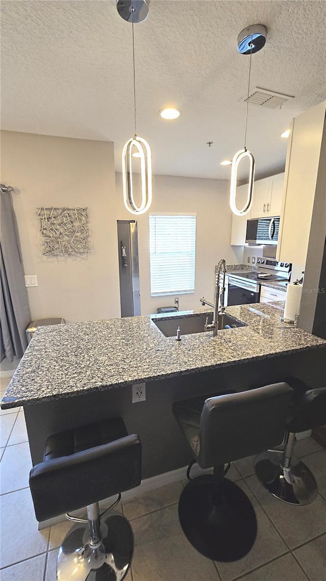136 Mcleods Way, Winter Springs, FL 32708 - kitchen with stainless steel range with electric cooktop, a breakfast bar area, a sink, a textured ceiling, and light tile patterned floors
