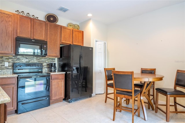 kitchen with visible vents, brown cabinetry, light stone counters, black appliances, and backsplash