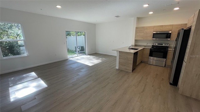 kitchen featuring light wood-type flooring, kitchen peninsula, sink, appliances with stainless steel finishes, and light brown cabinetry