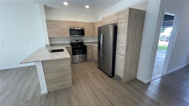 kitchen featuring stainless steel appliances, light stone countertops, light hardwood / wood-style floors, sink, and kitchen peninsula