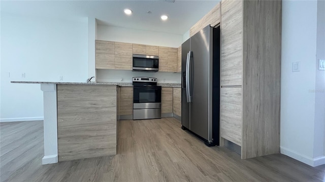 kitchen with light wood-type flooring, light stone countertops, appliances with stainless steel finishes, light brown cabinets, and a kitchen bar