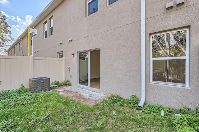rear view of property featuring stucco siding, fence, and central air condition unit