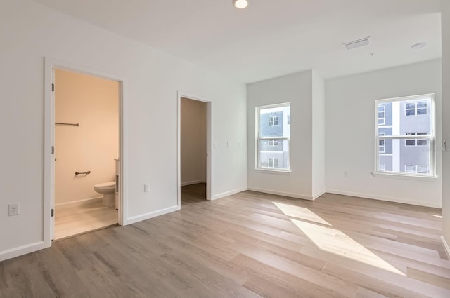 unfurnished bedroom featuring light wood finished floors, visible vents, baseboards, and connected bathroom