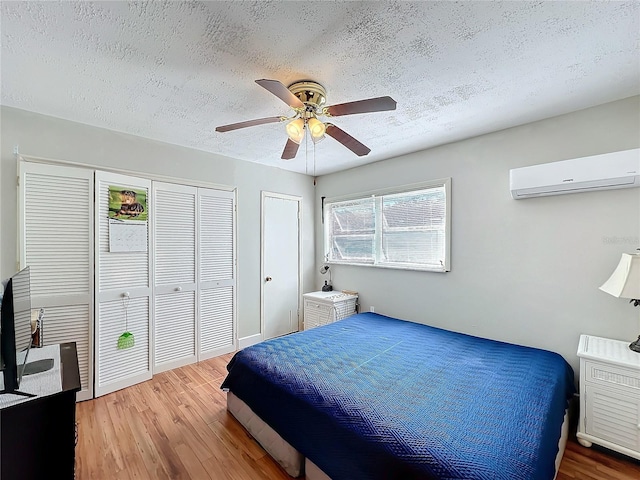 bedroom with hardwood / wood-style flooring, two closets, an AC wall unit, a textured ceiling, and ceiling fan