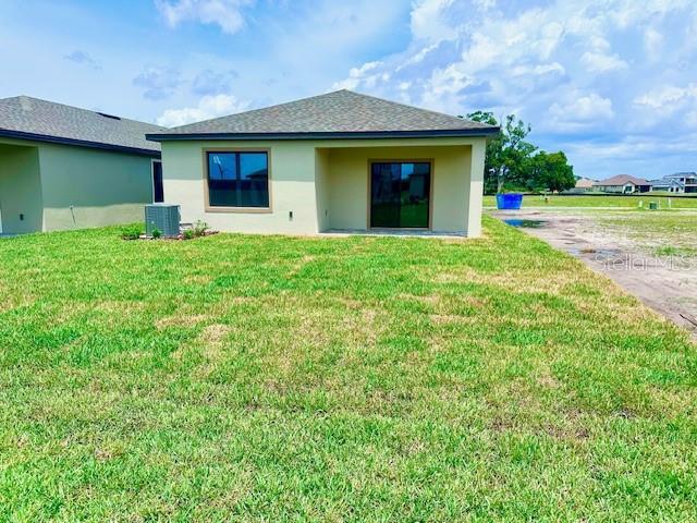 3225 Cup Dr, Lakeland, FL 33803 - back of property with stucco siding, a lawn, and cooling unit