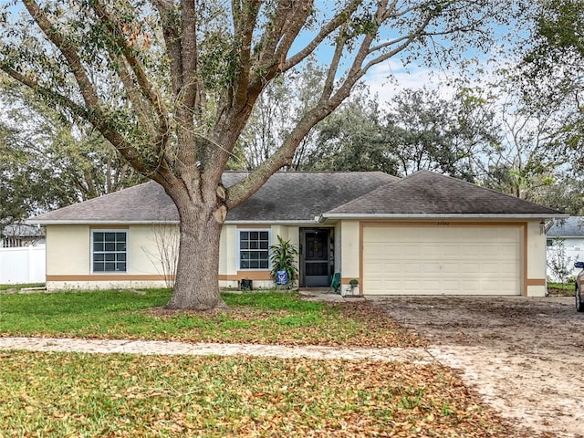 ranch-style home featuring a garage, a shingled roof, driveway, stucco siding, and a front lawn